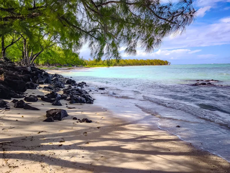 Quiet beach with black volcanic rocks and filao trees in Mauritius