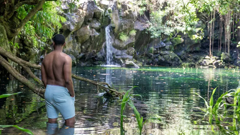 Un hombre en una poza bajo una cascada en el bosque, Mauricio