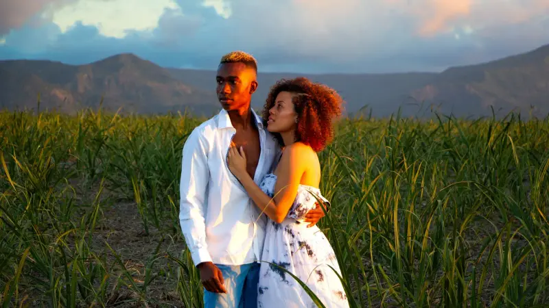 Una pareja en un campo de caña al atardecer, con montañas detrás, Mauricio
